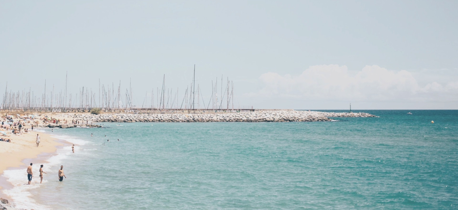 A bright blue sea and golden sandy beach with many people enjoying leisure activities.