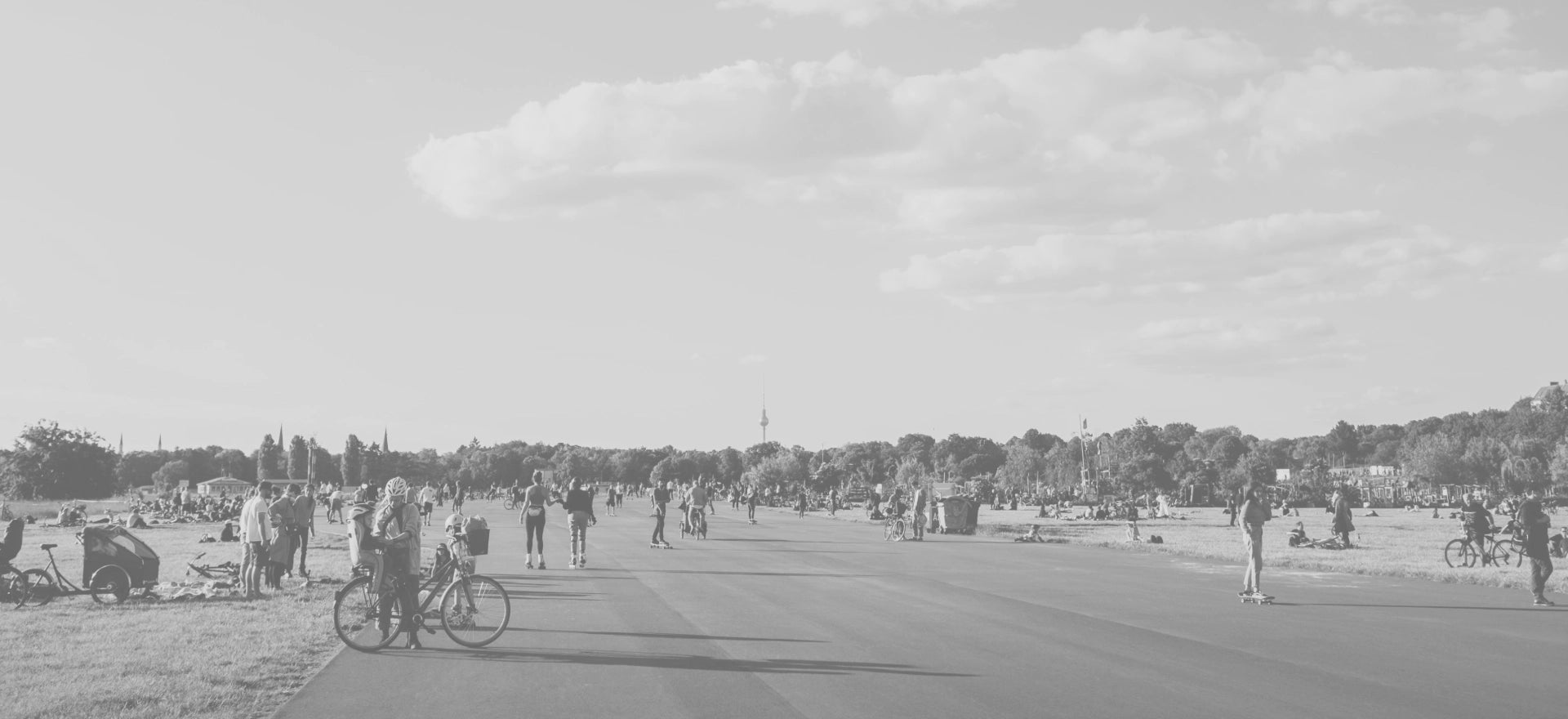 A wide road in Germany with flat grass lawns on both sides, where many people are relaxing outdoors.