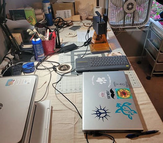 A corner of a workshop featuring an LP2 laser engraving machine on a desk alongside a laptop and keyboard used to operate it.
