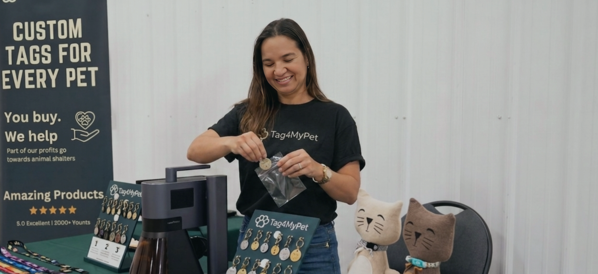 Eine Frau präsentiert personalisierte Haustieranhänger mit einer LaserPecker-Maschine an einem Stand auf einem Kunsthandwerksmarkt.
